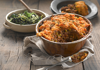 Spiced Cottage Pie served in a glass dish, with a dish of cabbage and a portion of the pie in a bowl