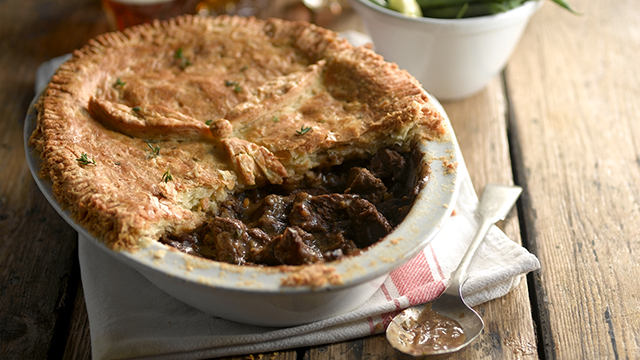 Beef and Chestnut Pie served in a white dish with some of the pastry removed to see the filling