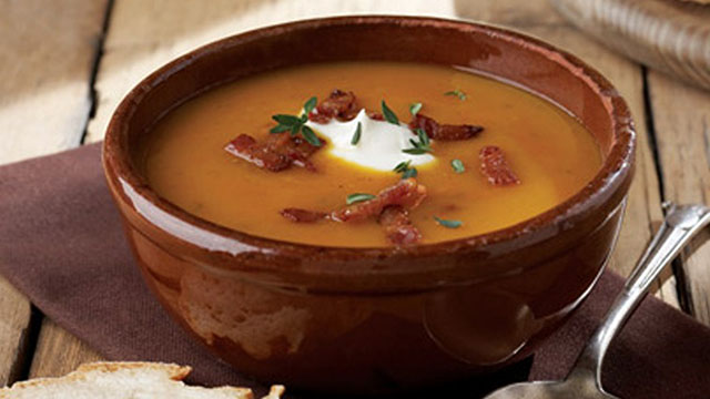 Butternut squash and smoked bacon soup served in a bowl topped with greek yoghurt and bacon bits