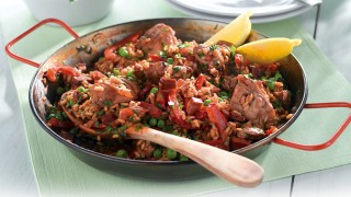 Chicken and chorizo paella served in the pan with lemon wedges and a sprinkling of parsley