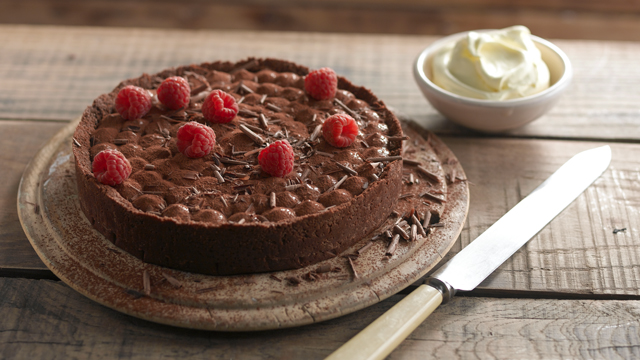 Rich Chocolate Mousse Torte dusted with cocoa, served on a board next to a bowl of whipped cream