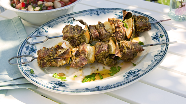 Pesto Marinated Lamb Kebabs served on a white and blue plate on an outdoor table