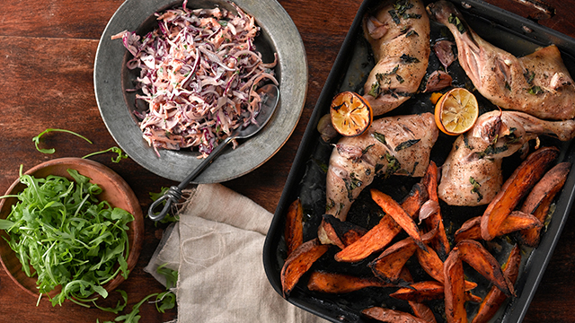 Lemon and Basil Roasted Chicken in a roasting tray with sweet potato wedges, coleslaw and rocket