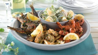 Bowl of mixed grilled fish including sardines, squid and king prawns with a bowl of new potato and runner bean salad