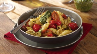 Penne pasta served with tomatoes, pesto, basil leaves in a grey dish