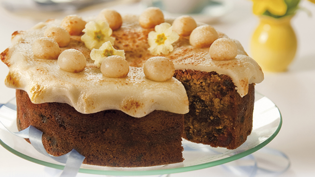 Simnel cake decorated with crystalised flowers, on a glass dish with a slice removed