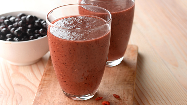 Purple passion smoothie served in two glasses, next to a bowl of blueberries