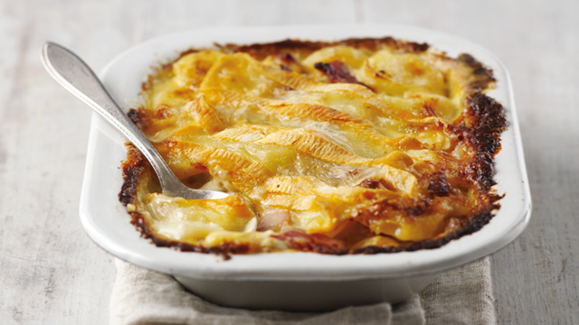 Tartiflette with Jersey Royals served in a white dish with a spoon placed in the dish