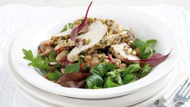 Warm chicken salad served in a white bowl with mixed leaves