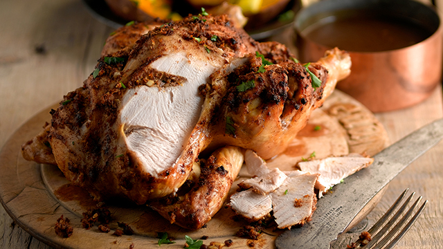 Winter Spiced Roast Chicken with a slice carved off, in front of a pan of gravy