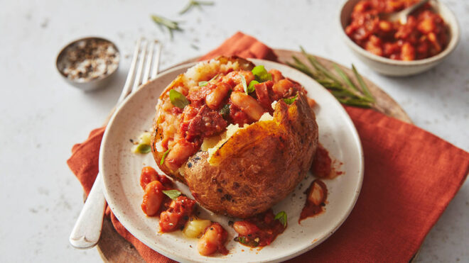 Baked potato with cannellini beans, chorizo and tomato filling, served on a white plate