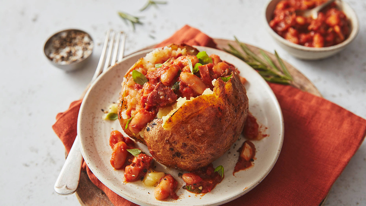 Baked potato with cannellini beans, chorizo and tomato filling, served on a white plate