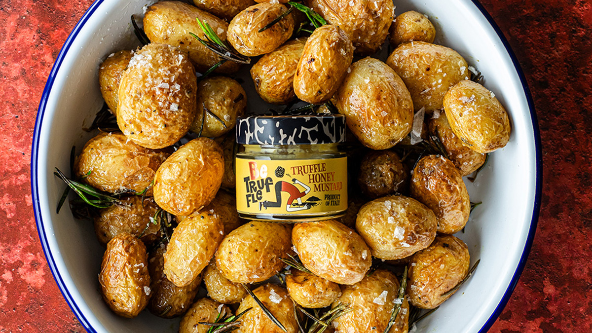 Zoomed in image of a bowl of seasoned potatoes with a pot of Be Truffle Honey Mustard in the middle