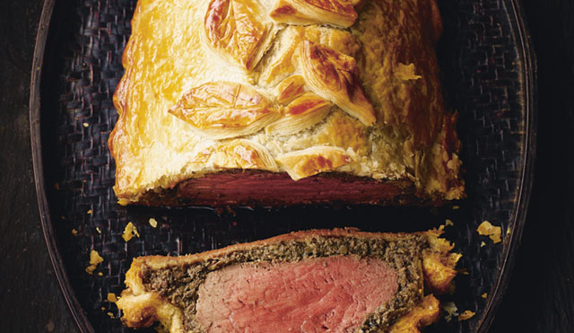 Beef Wellington served on a board, sliced to see the filling