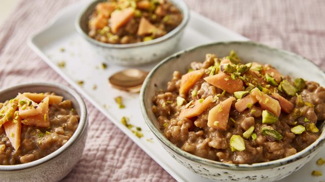 Chai Tea Rice Pudding served in white bowls, topped with pistachios and papaya slices