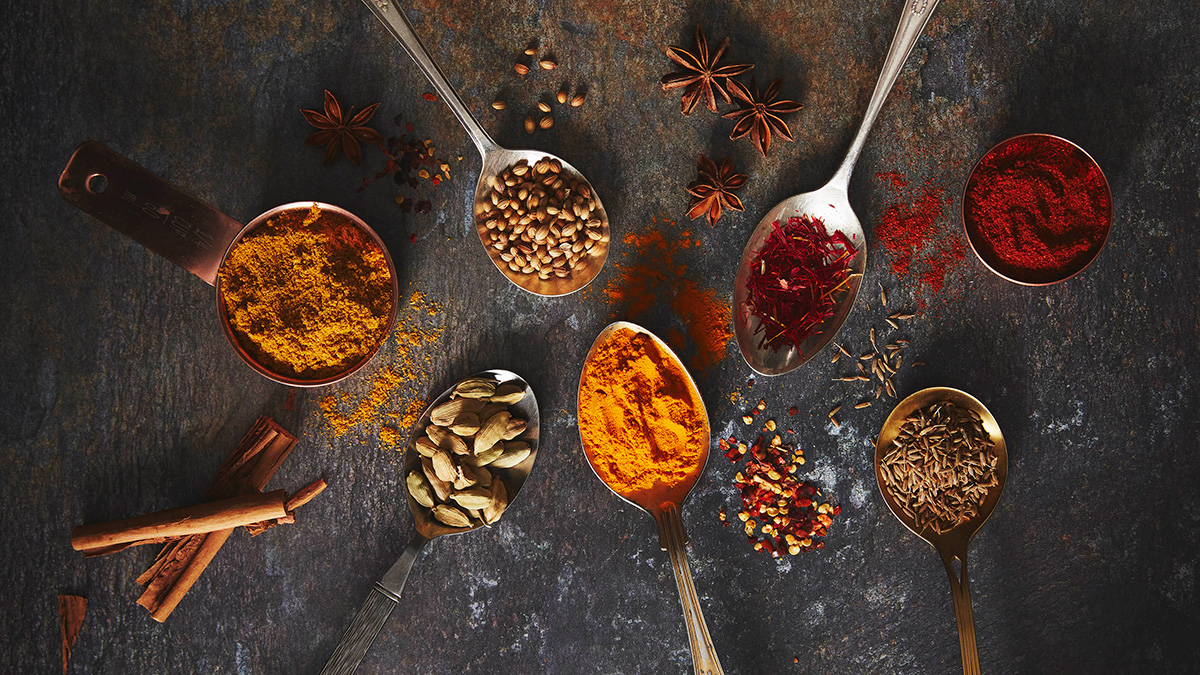 10 different spices laid out on different spoons against a dark background.