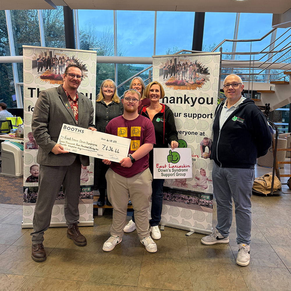 Image of a group of 6 people holding a large cheque in front of some ELDSSG banners
