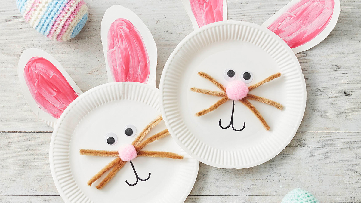 Image shows the completed craft which is two bunny faces made out of paper plates, pipe cleaners for whiskers, googly eyes and a drawn on mouth. Two ears poke out the top, painted pink in the middle.