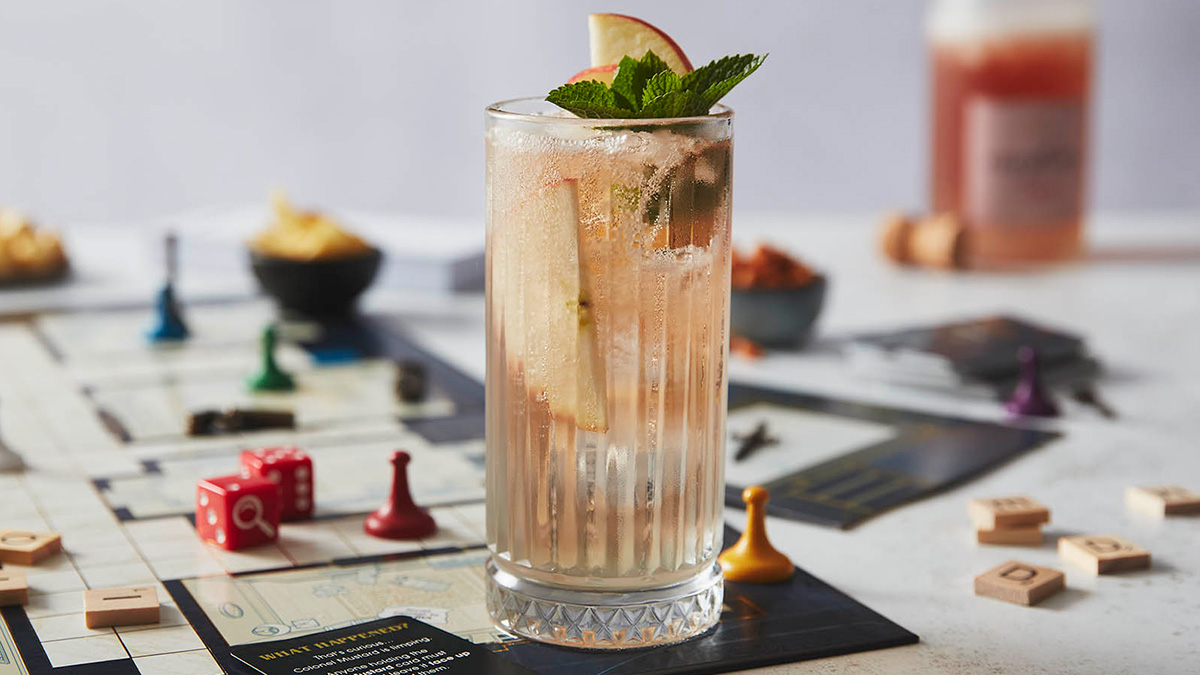 Mocktail in a tall glass with apple slices and mint leaves sat on a games board background