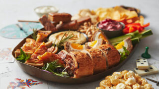 A platter with sausage rolls, dips, quiche, crudités, cake bites and popcorn.