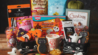 Halloween product table with Lancashire crisps, decorations, pumpkin and cat themed biscuits, a mug, 2 cat baskets and chocolate.