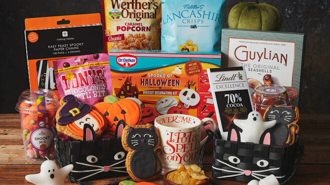 Halloween product table with Lancashire crisps, decorations, pumpkin and cat themed biscuits, a mug, 2 cat baskets and chocolate.