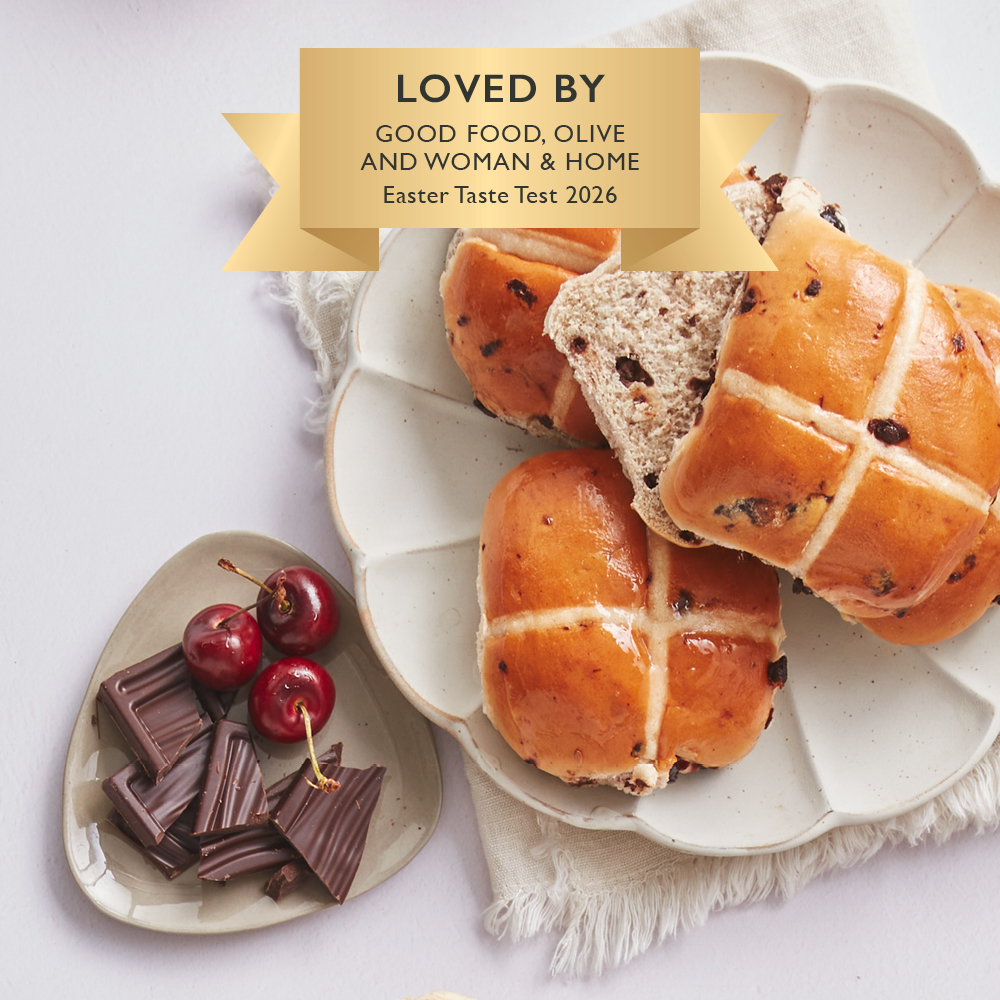 Image of a chocolate and sour cherry hot cross buns cut open on a plate next to some chocolate and cherries