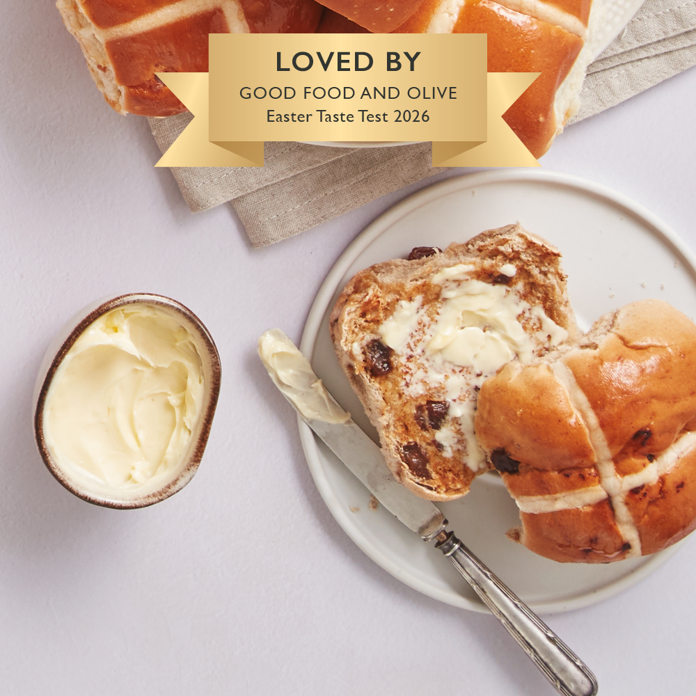 Image of a rich and fruity hot cross bun cut open on a plate with butter