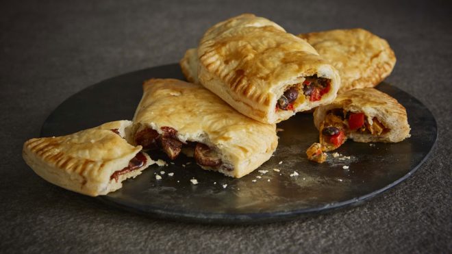 Butternut Squash, Peppers, Cheese and Beans Pasty served on a dark marble plate, sliced to see the filling
