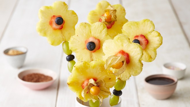 Six Fruit Flower Fondue Sticks served in a cup, with dipping sauces in the background