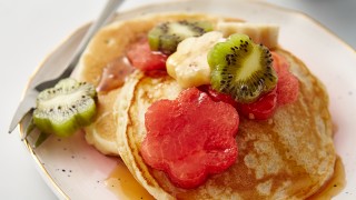 Mother's Day Pancakes served on a pale pink plate, with flower-shaped fruit and syrup