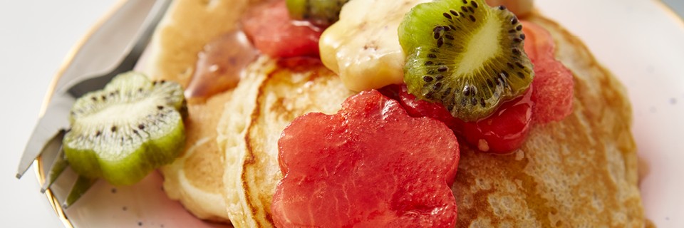 Mother's Day Pancakes served on a pale pink plate, with flower-shaped fruit and syrup