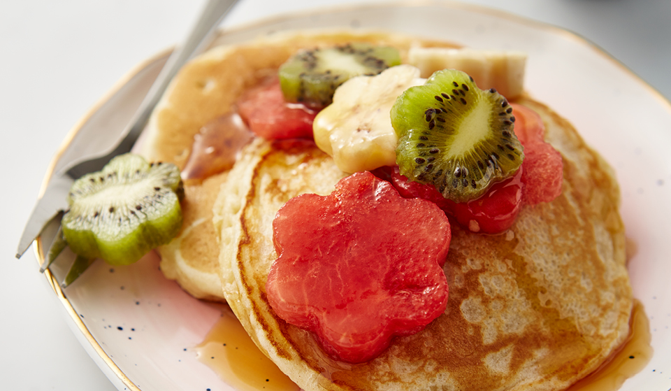Mother's Day Pancakes served on a pale pink plate, with flower-shaped fruit and syrup