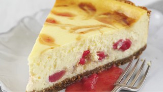 A slice of Baked Rhubarb and Orange Cheesecake with some rhubarb sauce on a plate with a dessert fork