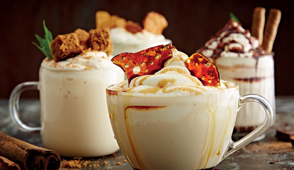 White Hot Chocolate served in glass cups with various toppings including caramel, cinnamon and biscuits