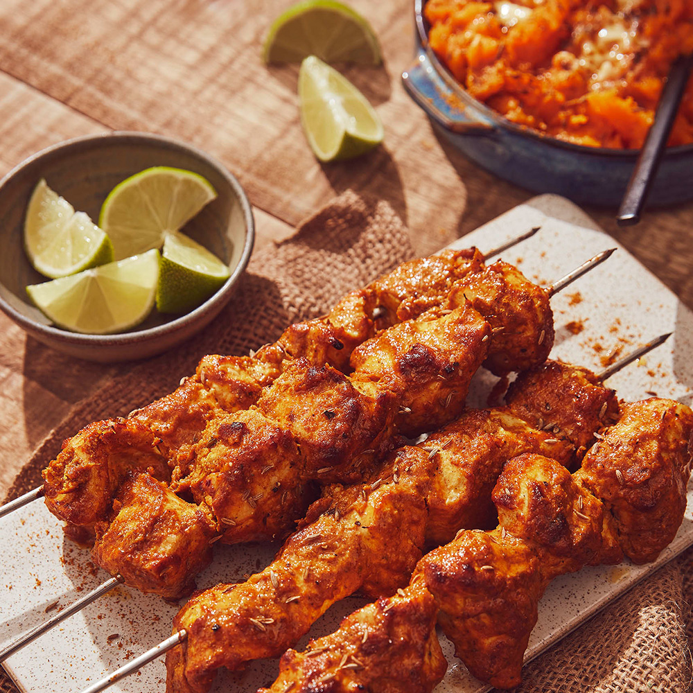 Image of 4 pheasant tikka kebabs on a plate next to a bowl of lime wedges and curried pumpkin mash