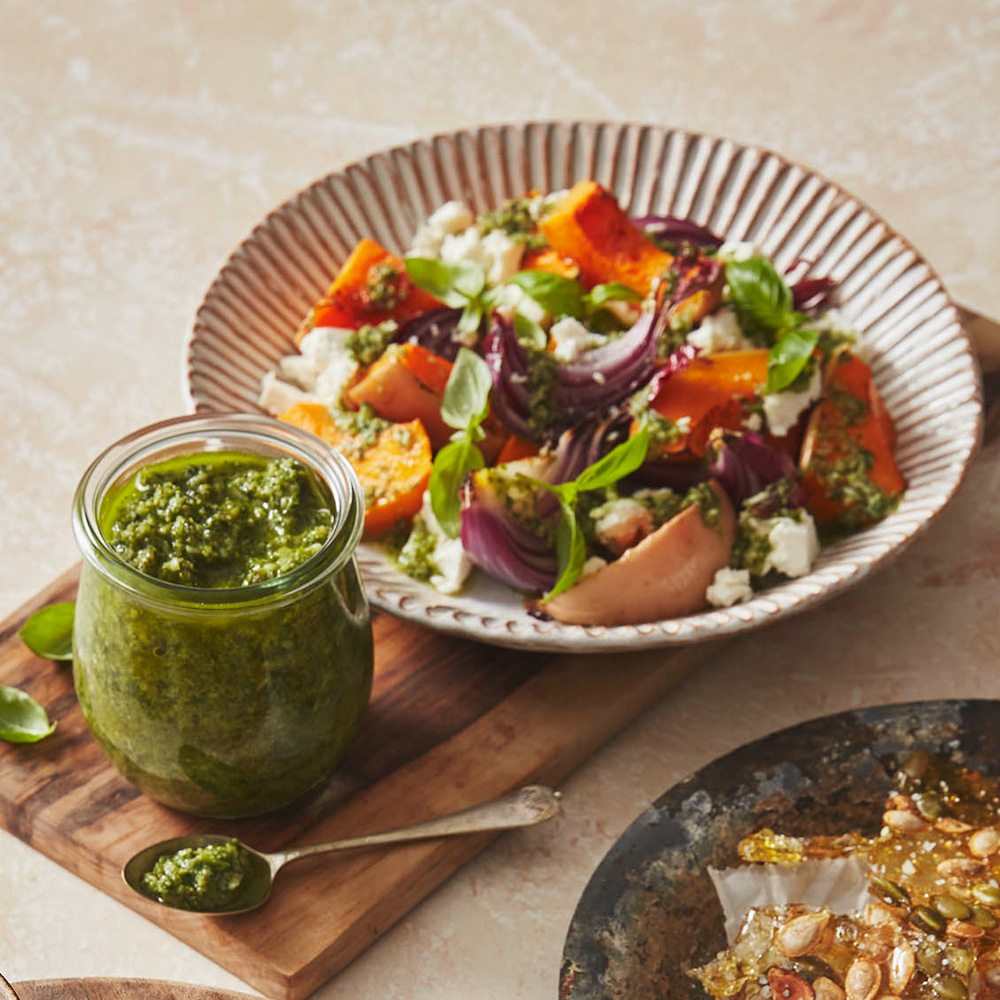 Image of a fresh, autumnal salad next to a jar of pumpkin seed pesto