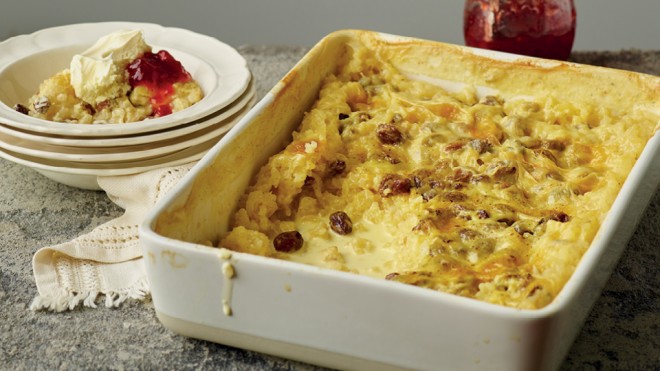 Claire's Milk Rice Pudding served in a white baking dish, with a portion placed in a bowl and topped with jam and cream