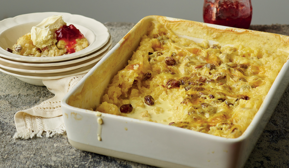 Claire's Milk Rice Pudding served in a white baking dish, with a portion placed in a bowl and topped with jam and cream