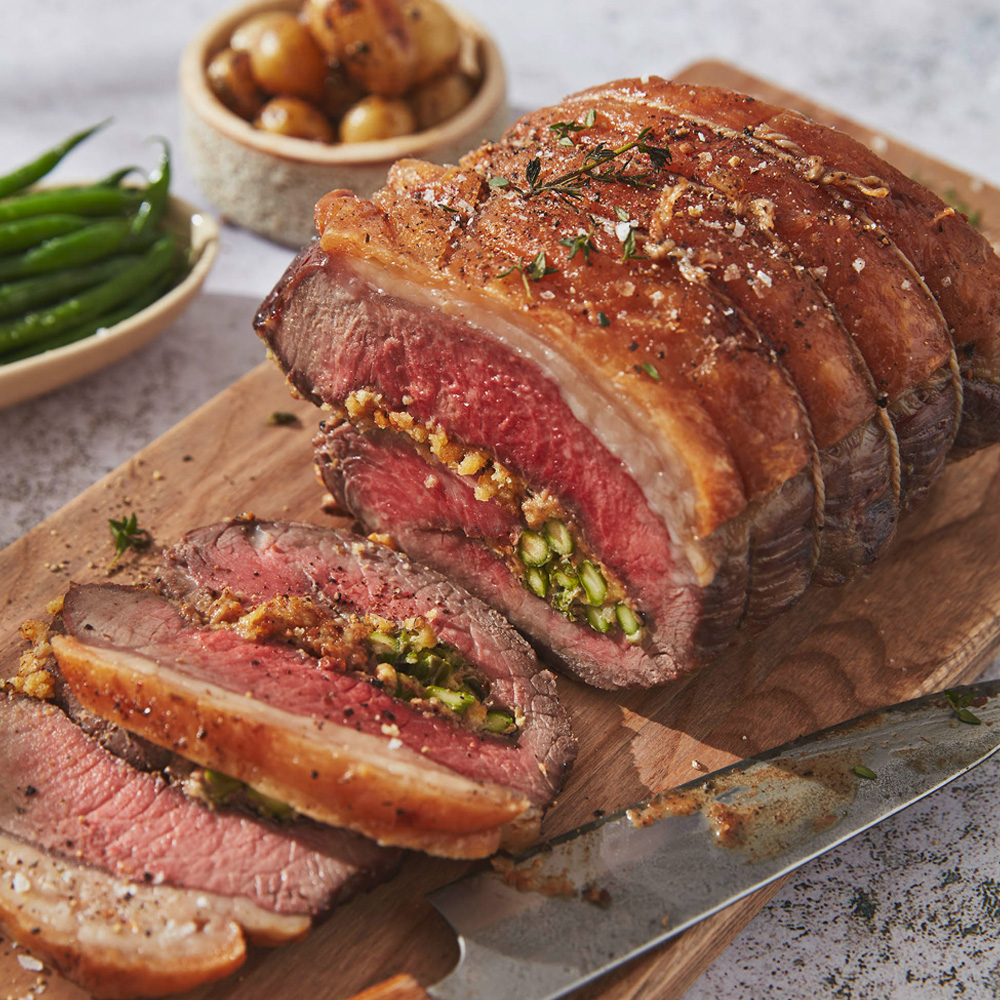 Image of an asparagus stuffed rolled sirloin joint on a wooden board with some slices that have been cut in front