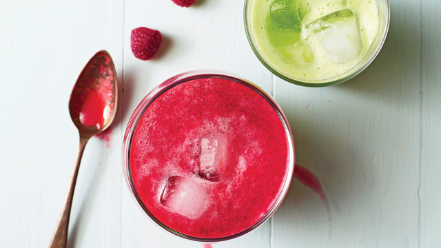 Raspberry Rush in a glass with ice next to a spoon and a couple of raspberries