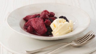 Summer Pudding with Clotted Cream Vanilla Ice Cream served in a white bowl with a fork and spoon to the side