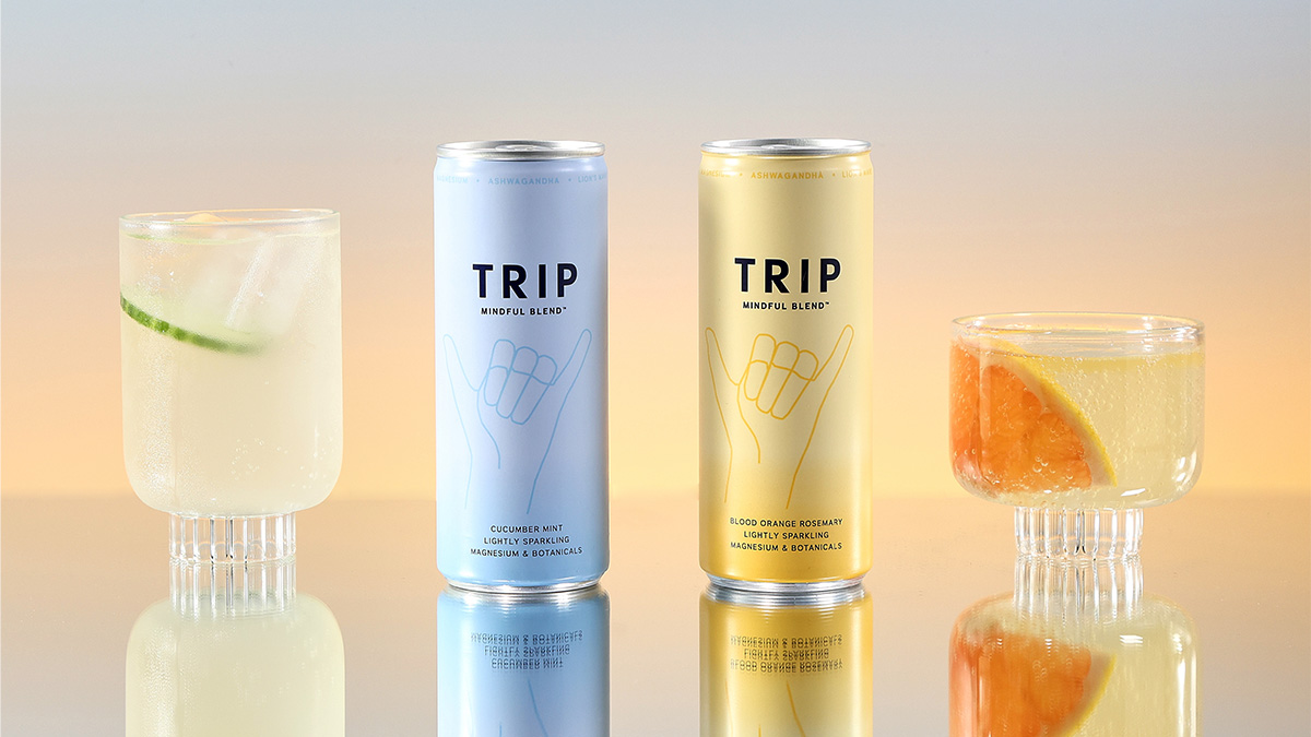 Image of two cans of Trip poured out into two glasses placed next to the cans on a mirrored table