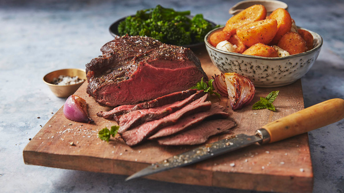 sliced venison should on a cutting board with roast potatoes in the background