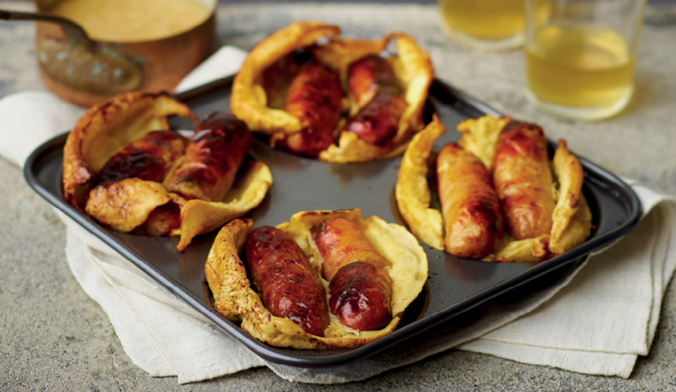 Toad-In-The Hole with a Twist served in a yorkshire pudding baking tray, on top of a white tablecloth