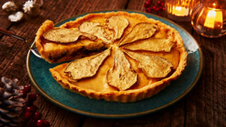 Festive Pear and Mincemeat Frangipane Tart, served on a blue plate with a slice being removed to see the filling