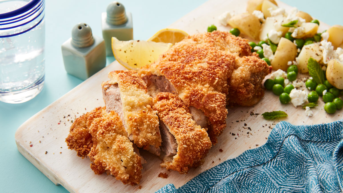 Almond Pork Schnitzel sliced and served on a wooden board with new potatoes and peas