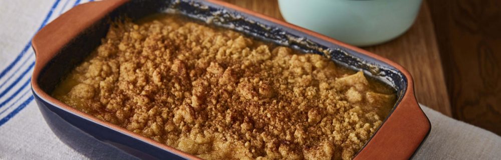 Salted Caramel Apple Crumble served in a blue dish, with a bowl of custard and a bowl of sauce behind