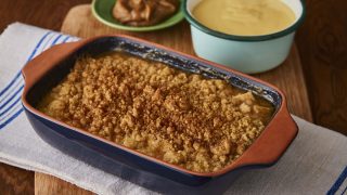 Salted Caramel Apple Crumble served in a blue dish, with a bowl of custard and a bowl of sauce behind