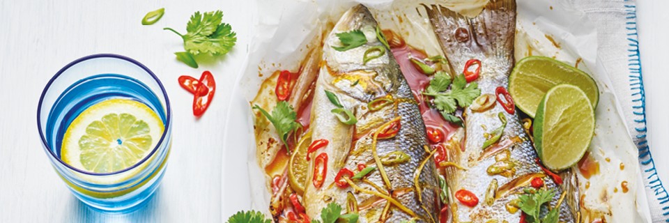 Asian Style Grilled Fish served on baking paper topped with coriander and lime wedges